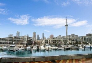 Ein Yachthafen mit vertäuten Booten, eine Stadtansicht mit modernen Gebäuden und einem markanten Turm.