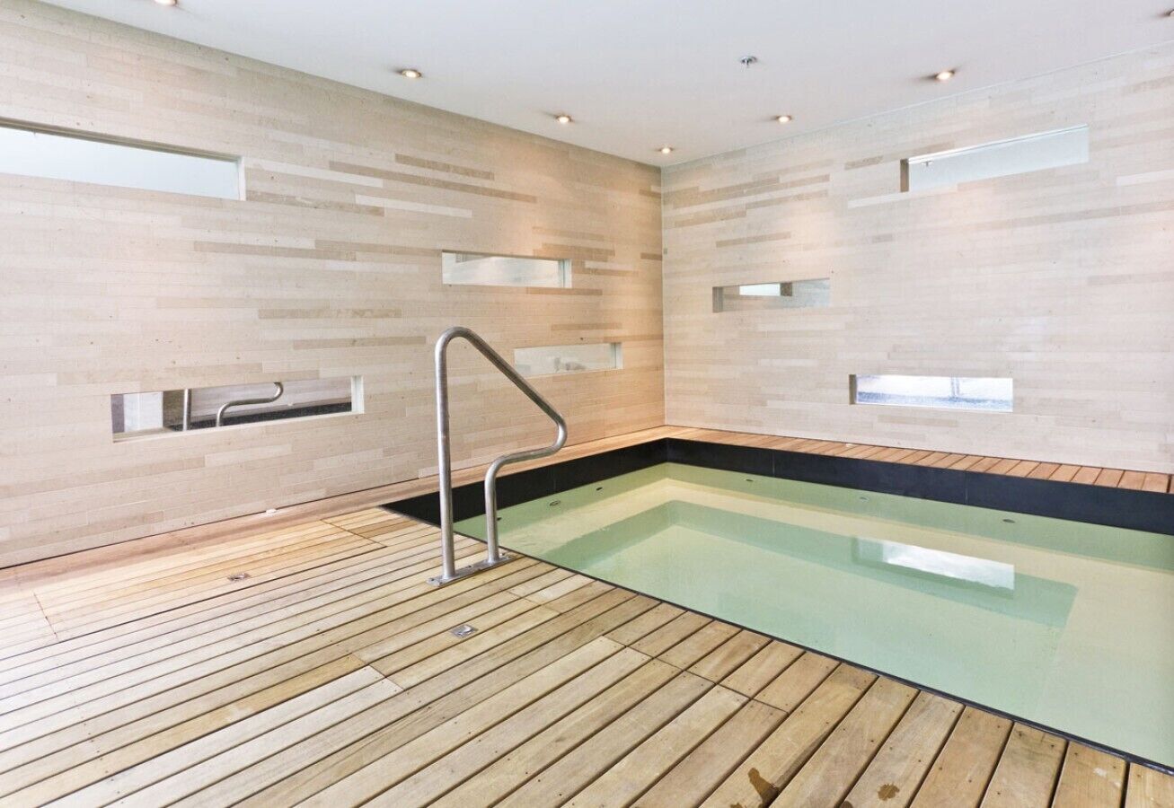 A modern indoor swimming pool with wooden flooring and a metal ladder.