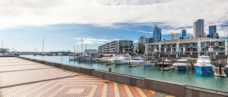 A marina with boats docked, a waterfront promenade, and modern buildings in the background.
