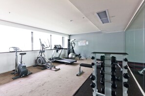 Une salle de sport équipée de tapis de course, de vélos elliptiques, d’un rameur et d’un banc de musculation.