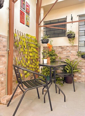 An outdoor patio with a metal table and chairs, surrounded by potted plants and a brick wall. - Charming 1BR Home Near Downtown SS & Metrocentro (San Salvador)