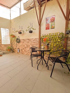 An outdoor patio with brick walls, hanging plants, metal chairs, and a table. - Charming 1BR Home Near Downtown SS & Metrocentro (San Salvador)