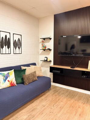 A modern living room with a blue sofa, decorative pillows, a flat-screen TV, and a wooden accent wall. - Charming 1BR Home Near Downtown SS & Metrocentro (San Salvador)
