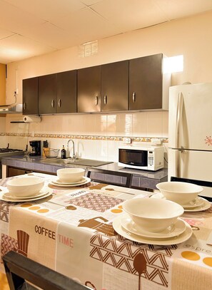 Une cuisine avec des meubles de couleur sombre, un réfrigérateur blanc, un four à micro-ondes et une table dressée avec de la vaisselle blanche.