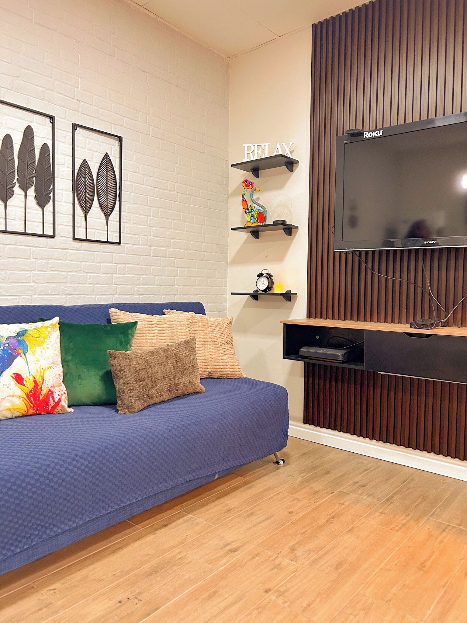 Ein modernes Wohnzimmer mit einem blauen Sofa, dekorativen Kissen, einem Flachbildfernseher und einer Wandpaneele aus Holz.