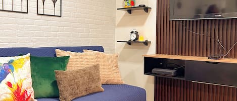 A modern living room with a blue sofa, decorative pillows, a flat-screen TV, and a wooden panel wall.
