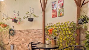 An outdoor patio with a brick wall, hanging plants, and a table with chairs. - Charming 1BR Home Near Downtown SS & Metrocentro (San Salvador)