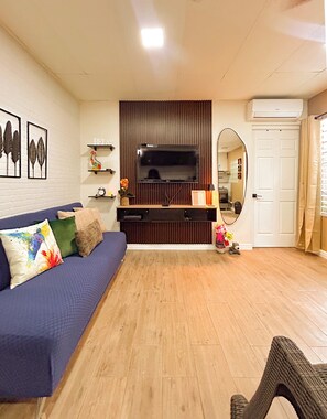 A living room with a blue sofa, a flat-screen TV, a wooden cabinet, and a mirror. - Charming 1BR Home Near Downtown SS & Metrocentro (San Salvador)