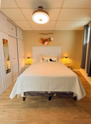 Une chambre à coucher comprenant un lit, deux tables de chevet, un luminaire suspendu, un radiateur et un élément décoratif mural.