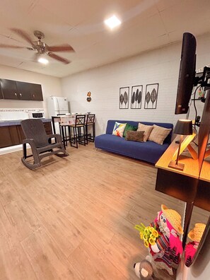 A living room with a sofa, a dining table, chairs, a ceiling fan, and a kitchen area with cabinets and appliances. - Charming 1BR Home Near Downtown SS & Metrocentro (San Salvador)