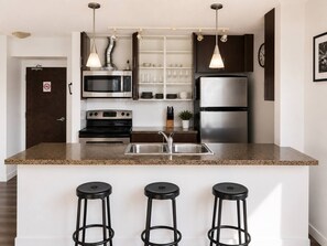 A modern kitchen with a granite countertop, stainless steel appliances, and three black stools. - Downtown Vancouver, Sleeps 7, Pool & Hot Tub (Vancouver)