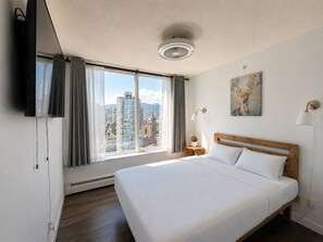 Ein Hotelzimmer mit einem großen Bett, einem Fernseher, Blick auf die Stadt und einem Bild an der Wand.