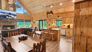 A spacious wooden interior with a dining area, kitchen, and a fireplace. - Spur and Arrow - Parade of Homes Cabin | Screened Porch and Hot Tub | Firepit (Morganton)