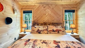 A bedroom with a wooden ceiling, two windows with curtains, a bed with a patterned bedspread, and two bedside lamps. - Spur and Arrow - Parade of Homes Cabin | Screened Porch and Hot Tub | Firepit (Morganton)