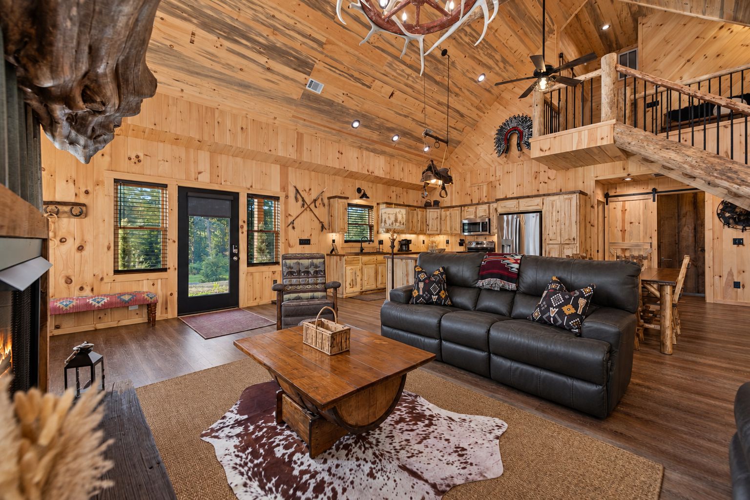 A rustic cabin interior with a fireplace, leather sofa, wooden dining table, and a kitchen area.