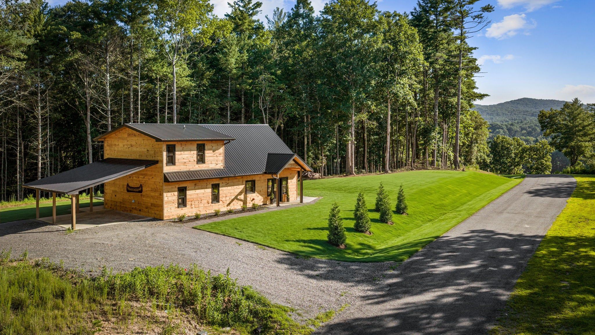 A two-story wooden house with a covered porch, surrounded by a well-maintained lawn and a forested area.