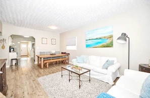 Ein Wohnzimmer mit einem weißen Sofa, einem Couchtisch und einem Gemälde an der Wand.