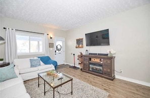 A living room with a white sofa, a glass coffee table, a wooden cabinet, and a mounted TV.