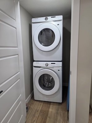 A laundry room with two stacked washing machines. - NEW 2-bedroom Basement Suite near Airport (Northeast)