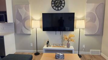 Ein Wohnzimmer mit einem Flachbildfernseher, zwei Wandlampen, einer Uhr und einer dekorativen Vase mit Blumen.