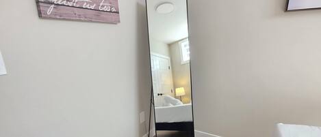 A bedroom with a large mirror, a fluffy rug, wooden flooring, and a bed with white bedding.