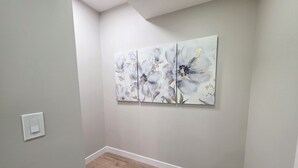 Ein Flur mit einer hellgrauen Wand, Holzdielen und einer weißen Fußleiste. An der Wand befindet sich ein weißer Lichtschalter.