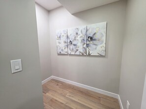 A hallway with a light gray wall, a wooden floor, and a white baseboard. There is a white light switch on the wall. - NEW 2-bedroom Basement Suite near Airport (Northeast)