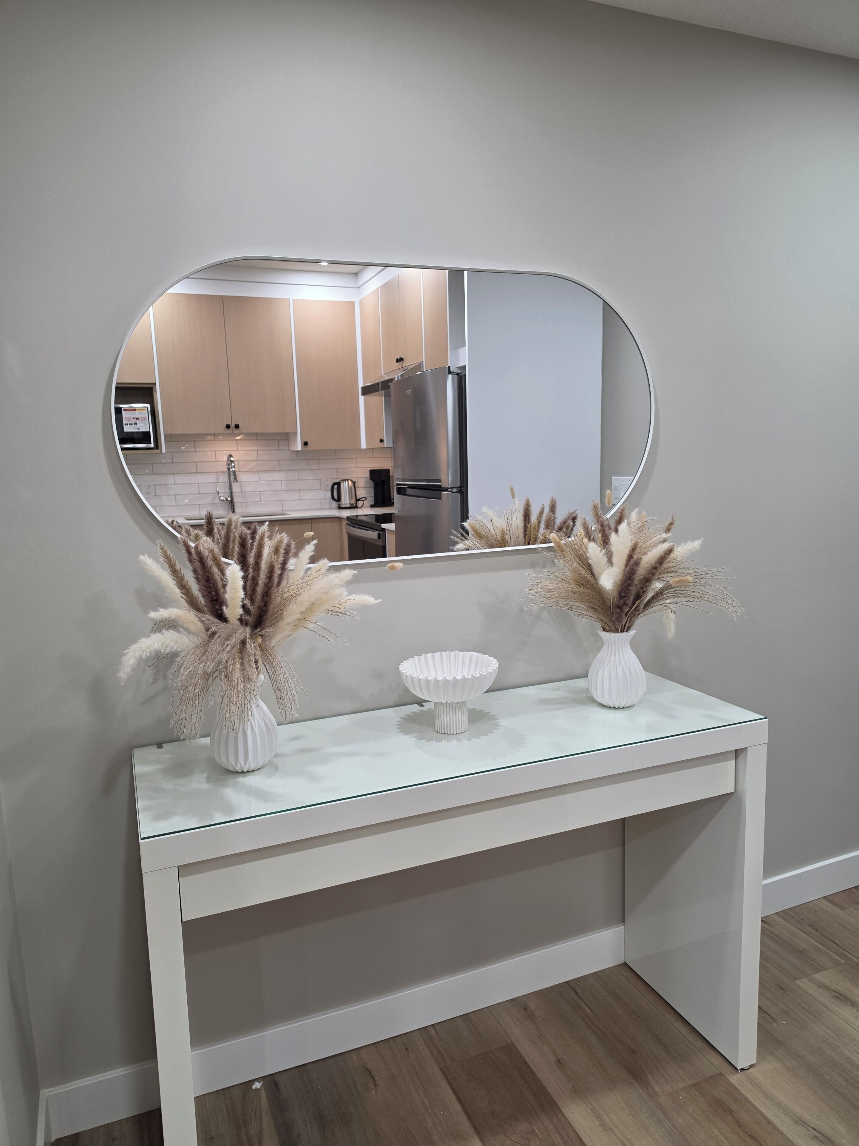 Een witte console tafel met twee witte vazen en een grote ovale spiegel erboven.