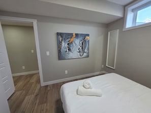 A bedroom with a bed, a painting on the wall, and a window. - NEW 2-bedroom Basement Suite near Airport (Northeast)