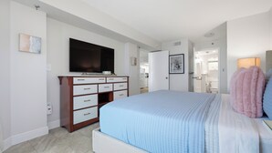 Una camera da letto con un letto, una cassettiera, una televisione e un bagno visibile attraverso una porta aperta.