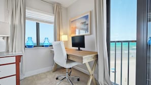Habitación de hotel con escritorio, computadora y vista a la playa.