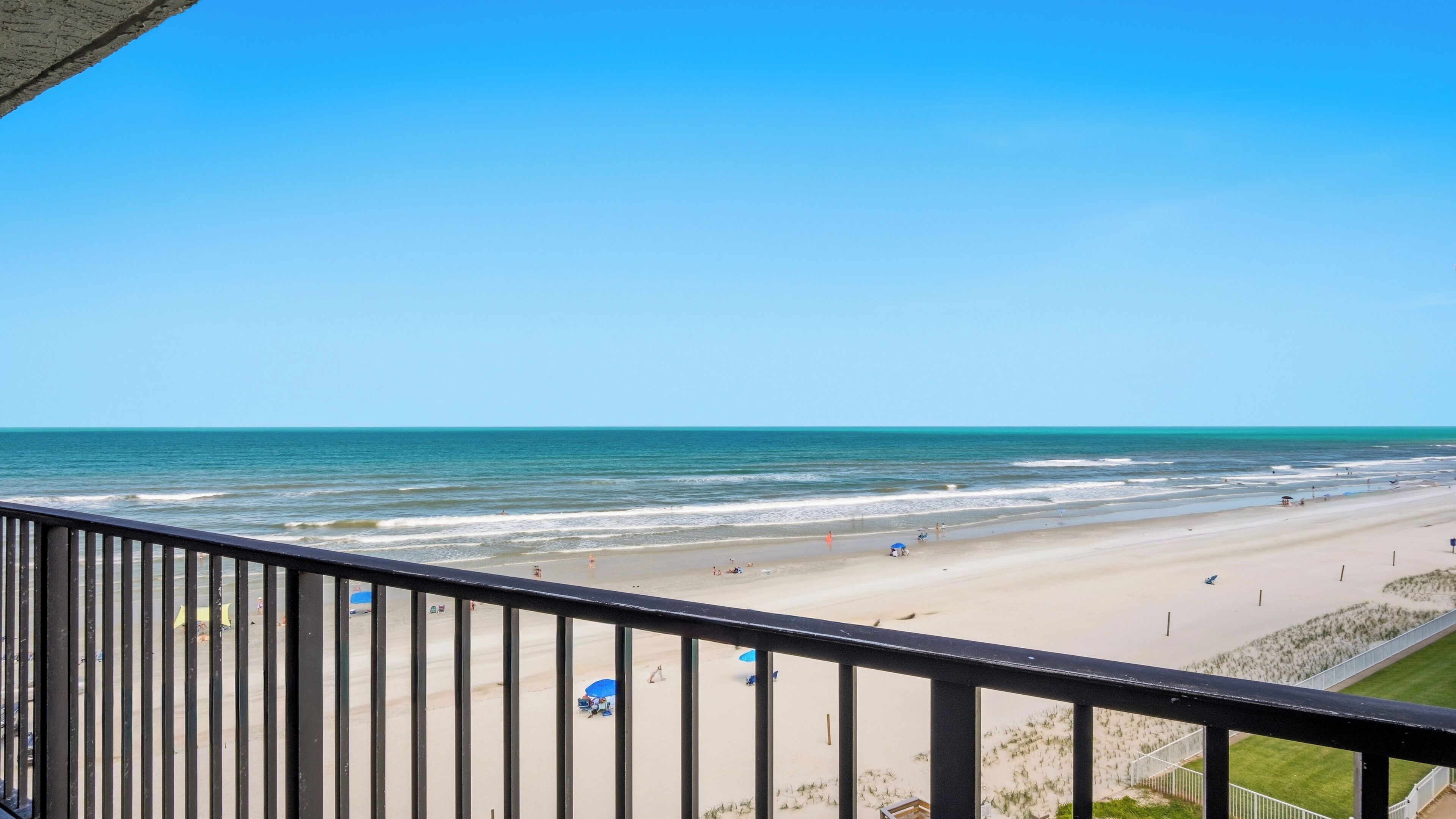 A beach view from a balcony with a railing, sandy beach, and ocean.