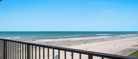 A beach view from a balcony with a railing, sandy beach, and ocean.