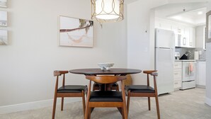 Zona pranzo con tavolo rotondo, due sedie, una lampada a sospensione e una cucina sullo sfondo.