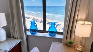 A room with a view of a beach, two blue vases on a windowsill, a lamp, and a small plant. - Ocean Trillium 604 - Beautiful Beachfront Condo in New Smyrna Beach with Oceanfront Pool (New Smyrna Beach)