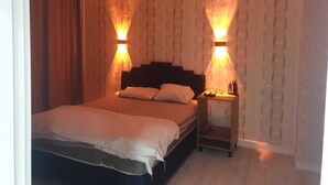 A hotel room with a bed, two wall-mounted lights, a nightstand, and a curtain.