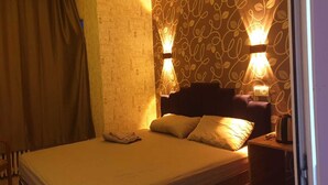 A hotel room with a bed, a chair, a nightstand, and a wall with decorative lighting.