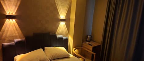 A hotel room with a bed, two wall-mounted lamps, a wooden nightstand, a chair, and a curtain.