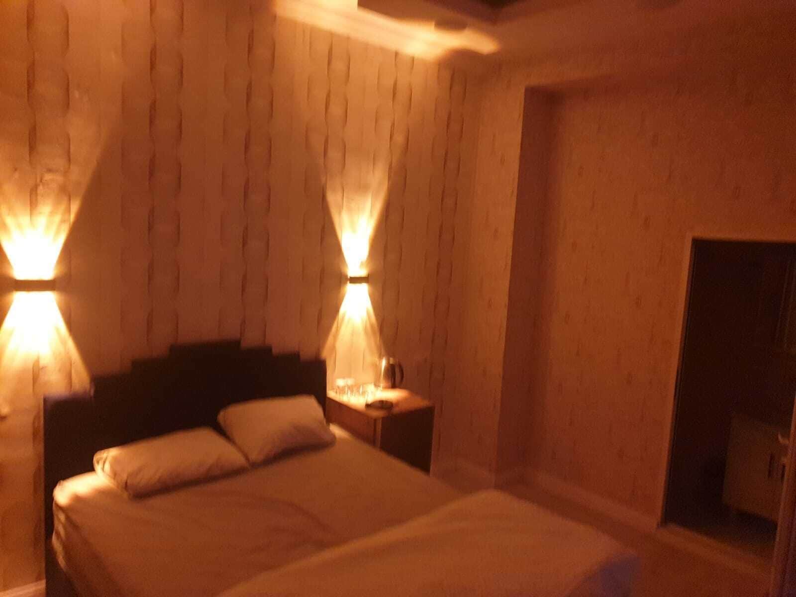 Una habitación con cama, mesitas de noche y lámparas fijadas a la pared.