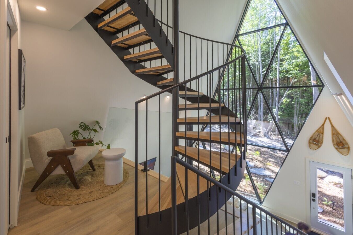 A modern interior with a spiral staircase, a round rug, a chair, and a plant.