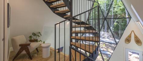 Un intérieur moderne avec un escalier en colimaçon, un tapis rond, une chaise et une plante.