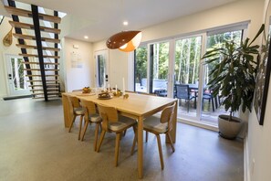 A dining area with a wooden table and chairs, a pendant light, and a large window with a view of trees. - NordAstra | SPA | Accès au Lac (Chertsey)