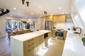 A modern kitchen with a central island, stainless steel appliances, and a dining area with natural light. - NordAstra | SPA | Accès au Lac (Chertsey)