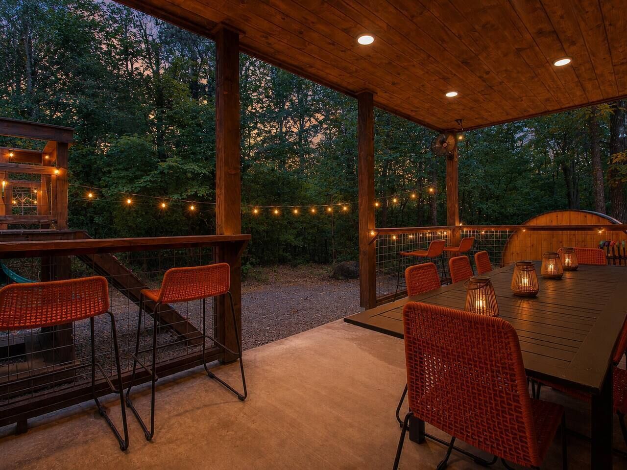 An outdoor patio with a wooden deck, wicker chairs, a table, and string lights.