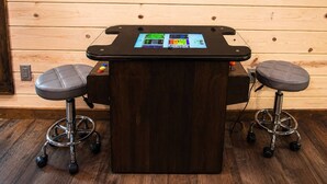 Eine Bar mit einer dunklen Holztheke, zwei Barhocker und einem Bildschirm, der verschiedene Bedienelemente zeigt.
