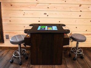 A bar area with a dark wooden bar counter, two stools, and a digital screen displaying various controls. - 5BR Cabin + Glamping Dome | Sauna, ATV Trails, Pickleball (Broken Bow)