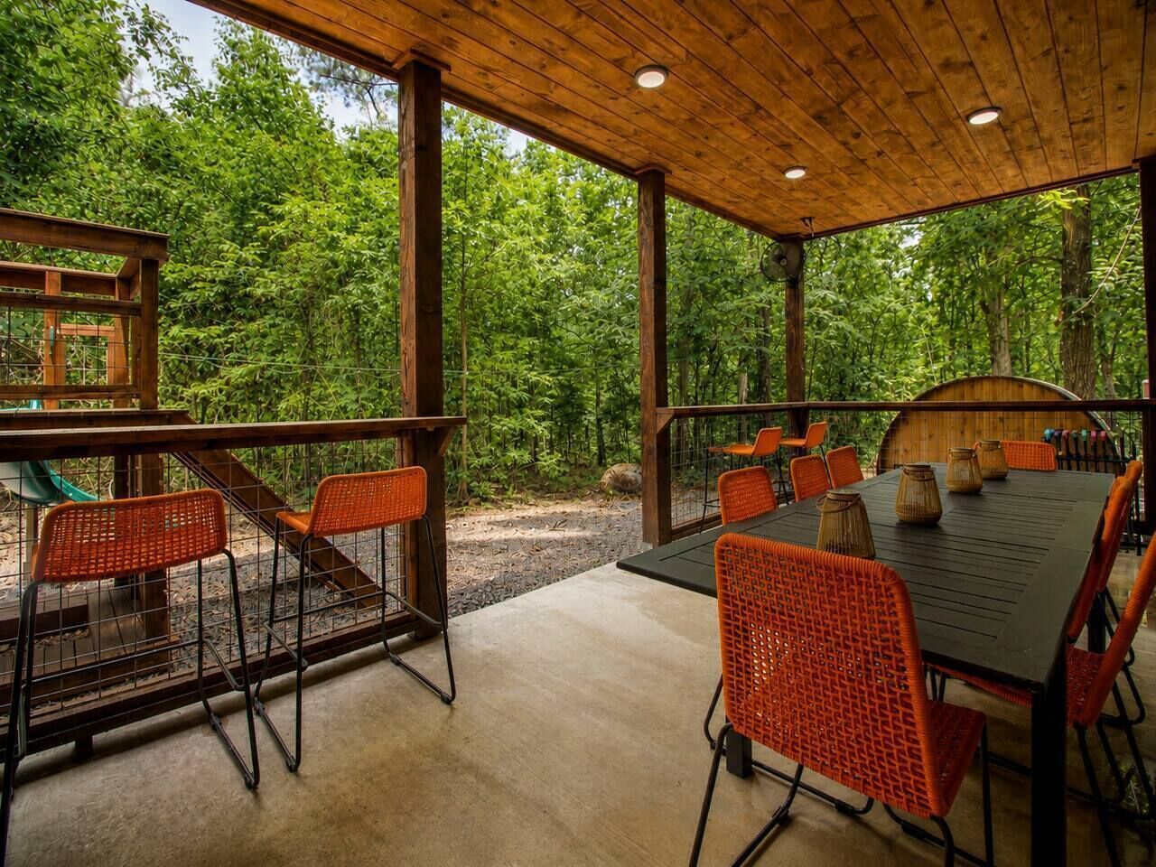 An outdoor patio with a table and chairs, surrounded by a wooden fence and lush greenery.