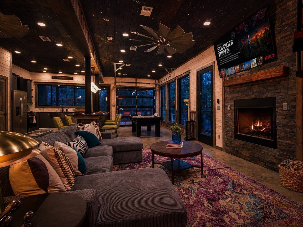A modern living room with a fireplace, a large TV screen, and a cozy seating area.
