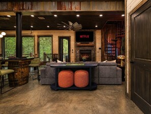 A cozy living room with a fireplace, a Netflix sign, and a large window overlooking greenery. - 5BR Cabin + Glamping Dome | Sauna, ATV Trails, Pickleball (Broken Bow)