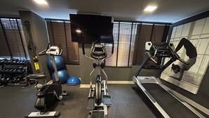 A gym with exercise equipment including a stationary bike, elliptical, treadmill, and weights. - Stgo Metro A. Hurtado - Domus Travels (Santiago)